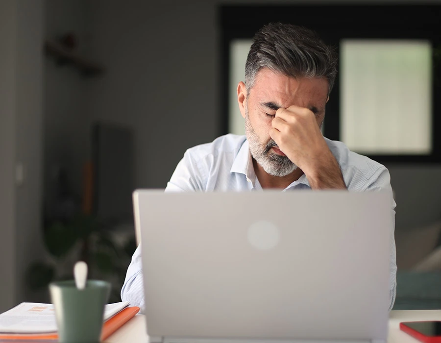Man met burn-out zit achter laptop en wrijft vermoeid over zijn ogen.