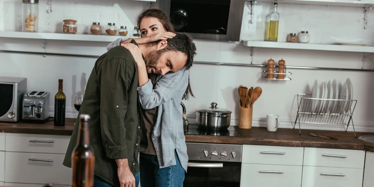 Vrouw troost man met alcohol en relatieproblemen in keuken setting.