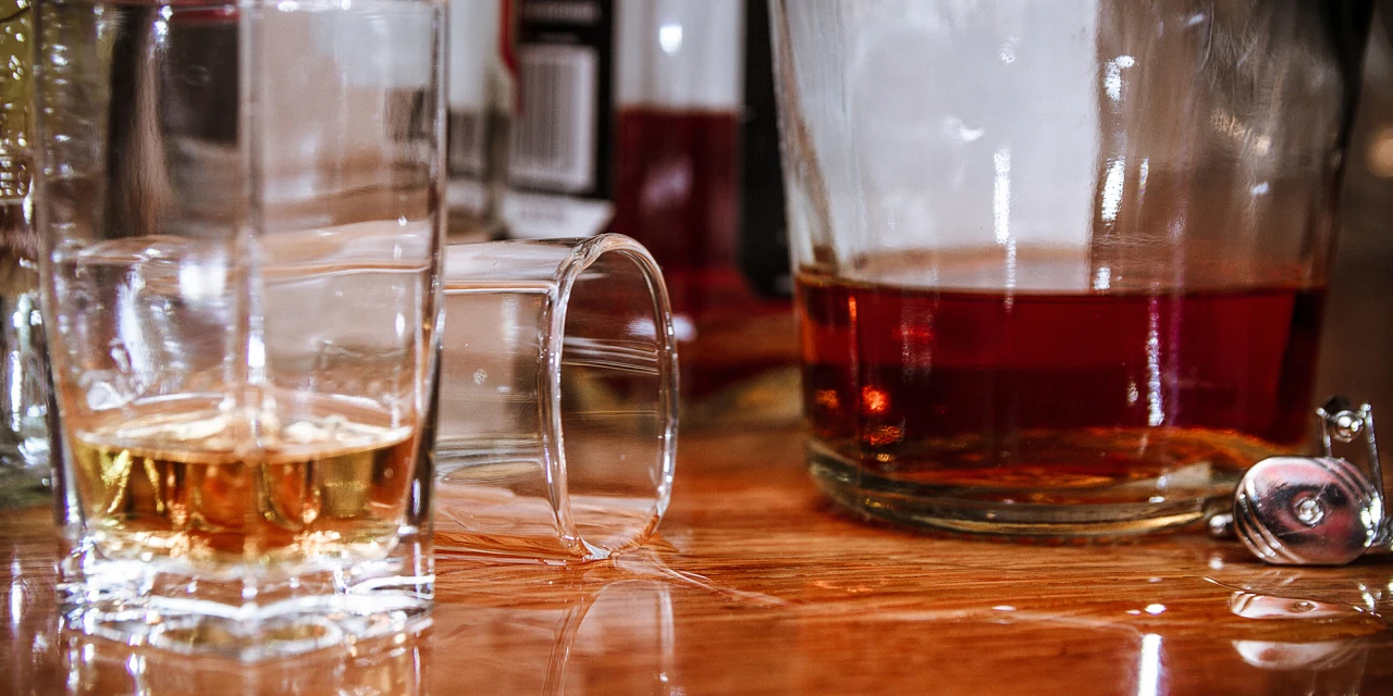 Omgevallen glas en fles sterke drank op tafel wat is alcoholvergiftiging.