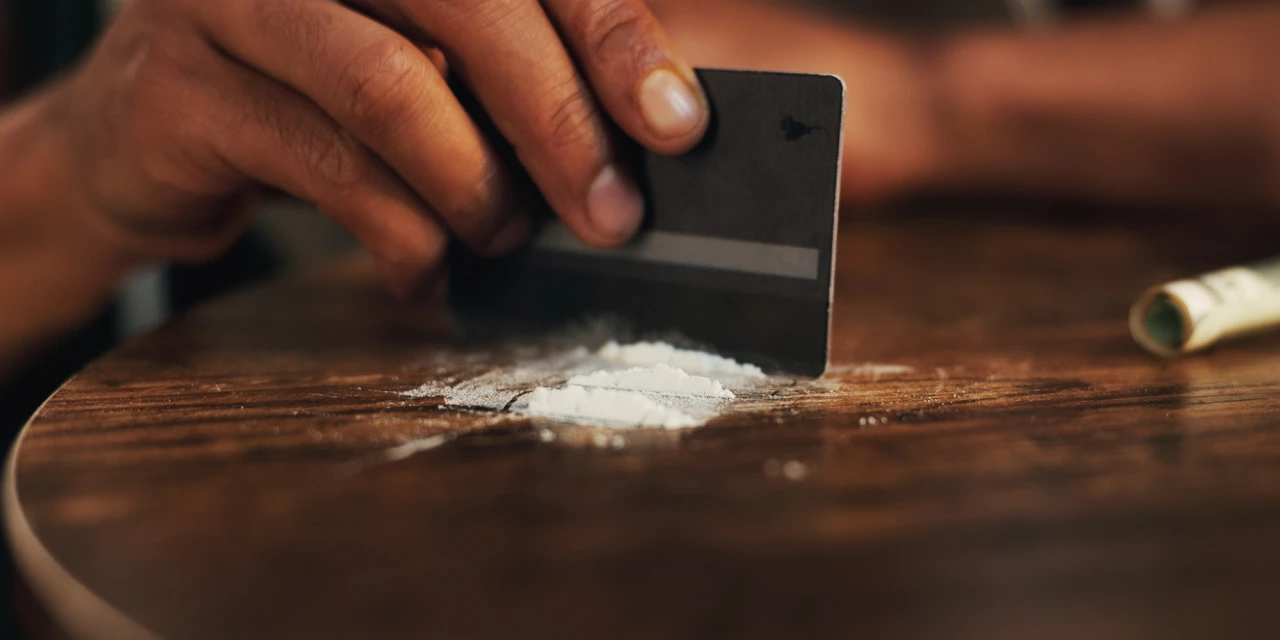 Hand verdeelt wit poeder op tafel met pasje en denkt aan stoppen met coke.