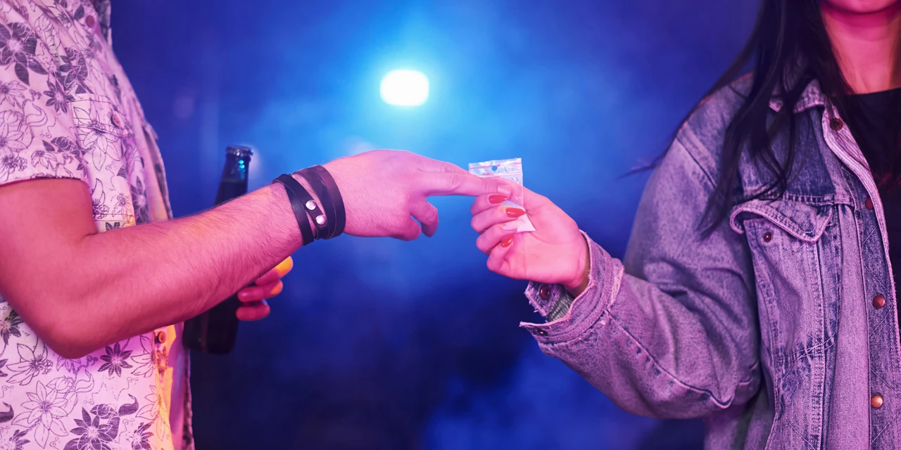 Handen wisselen zakje drugs op feest, wijst op designerdrugsverslaving in clublicht.