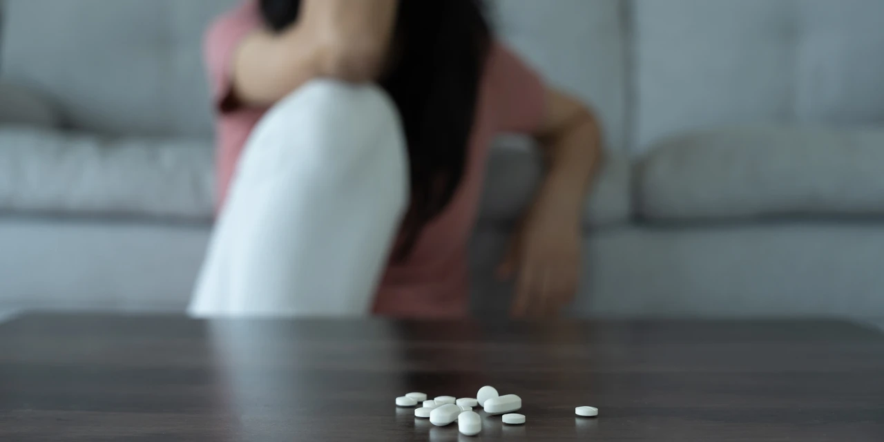 Persoon zit somber op bank met pillen op tafel symbool voor medicijnverslaving.