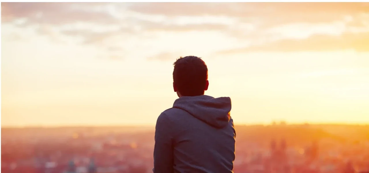 Achteraanzicht van een man in een grijs vest die naar de zonsondergang kijkt. 