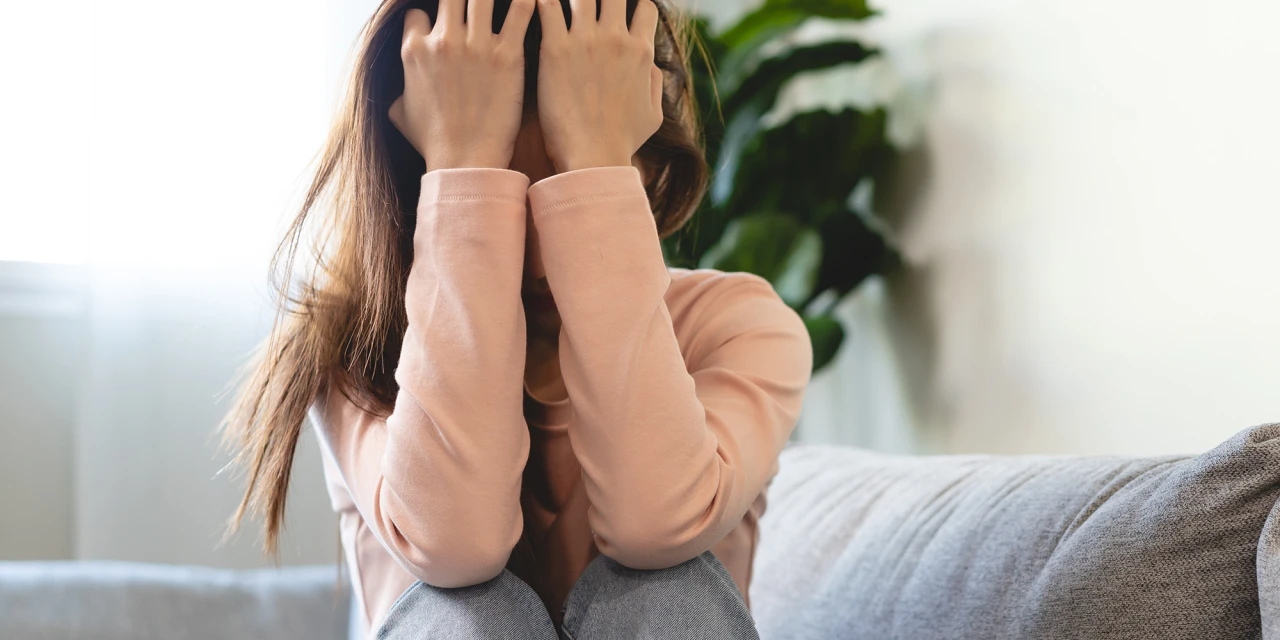 Persoon zit op bank met handen in haar worstelend met designerdrugsverslaving.