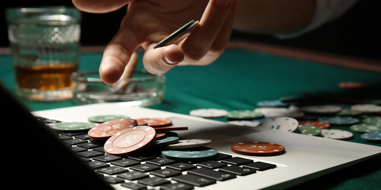 Hand met pokerchips boven laptop toont gedragsverslaving en online gokken.