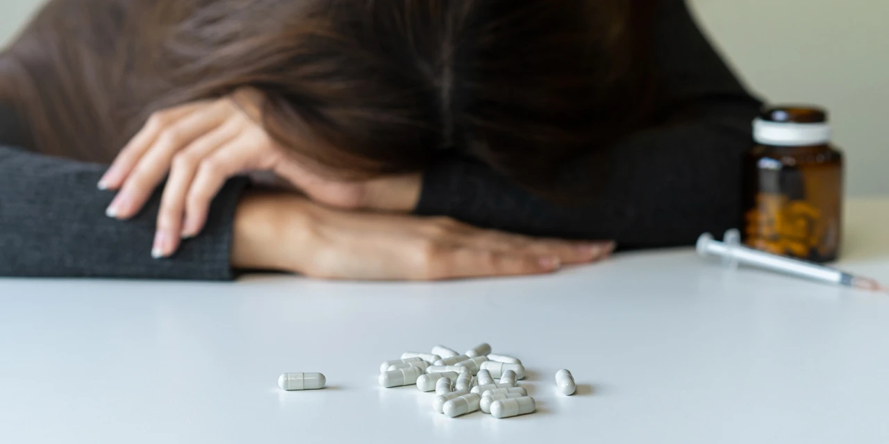 Persoon ligt uitgeput naast pillen en spuit symbool voor opioïdenverslaving.