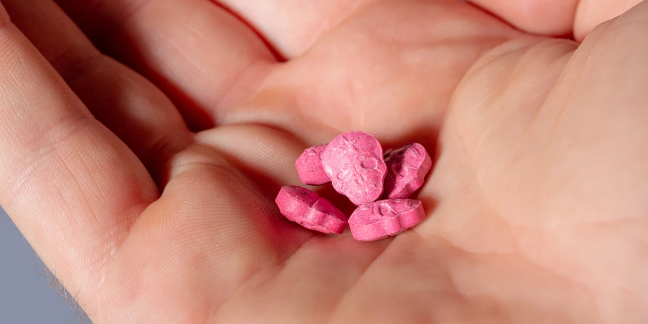 Roze pillen liggen in open hand als teken van MDMA-verslaving.