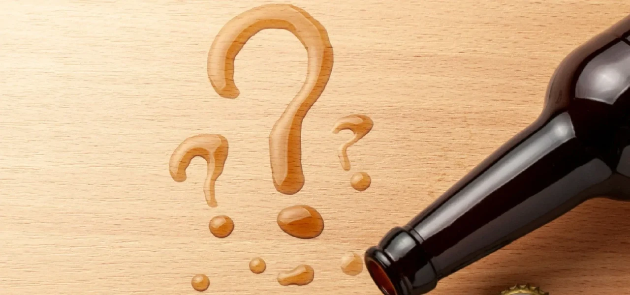 vraagtekens-getekend-met-drank Vraagtekens op houten ondergrond getekend met drank, met daarnaast een flesje drank.