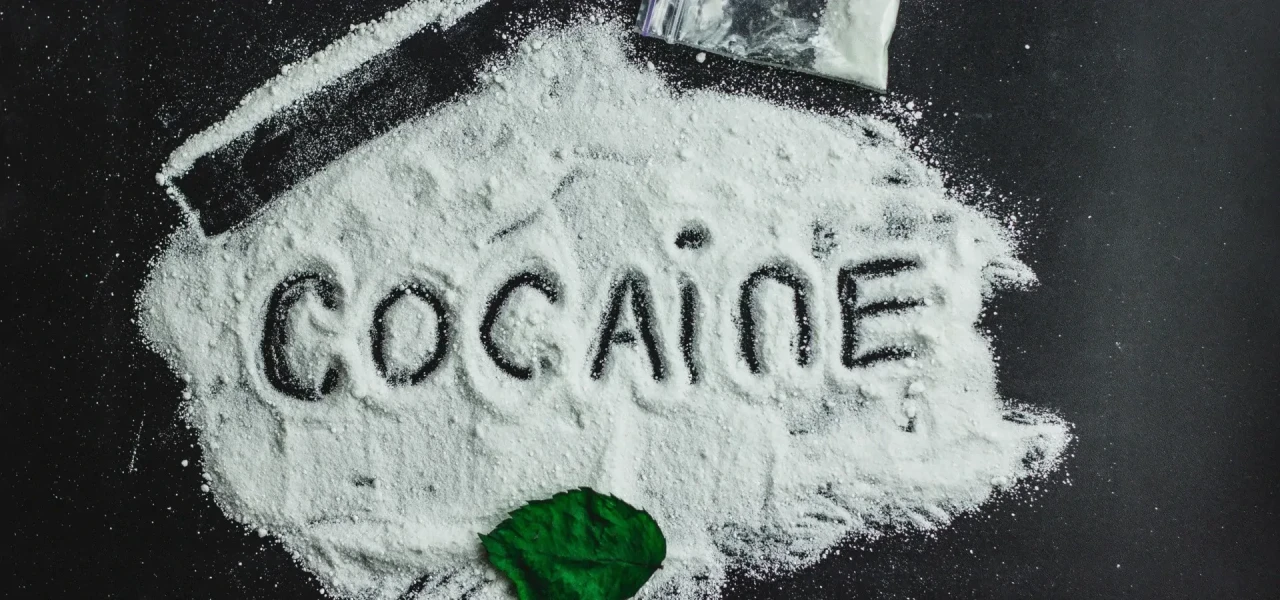 Op een donkere achtergrond ligt coke in de vorm van wit poeder, waarin 'cocaine' is geschreven. 
