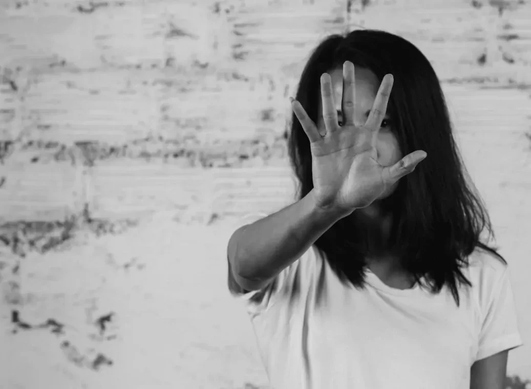 Zwart-wit foto van een vrouw die gebaart te stoppen met haar hand in de lucht en voor haar gezicht.