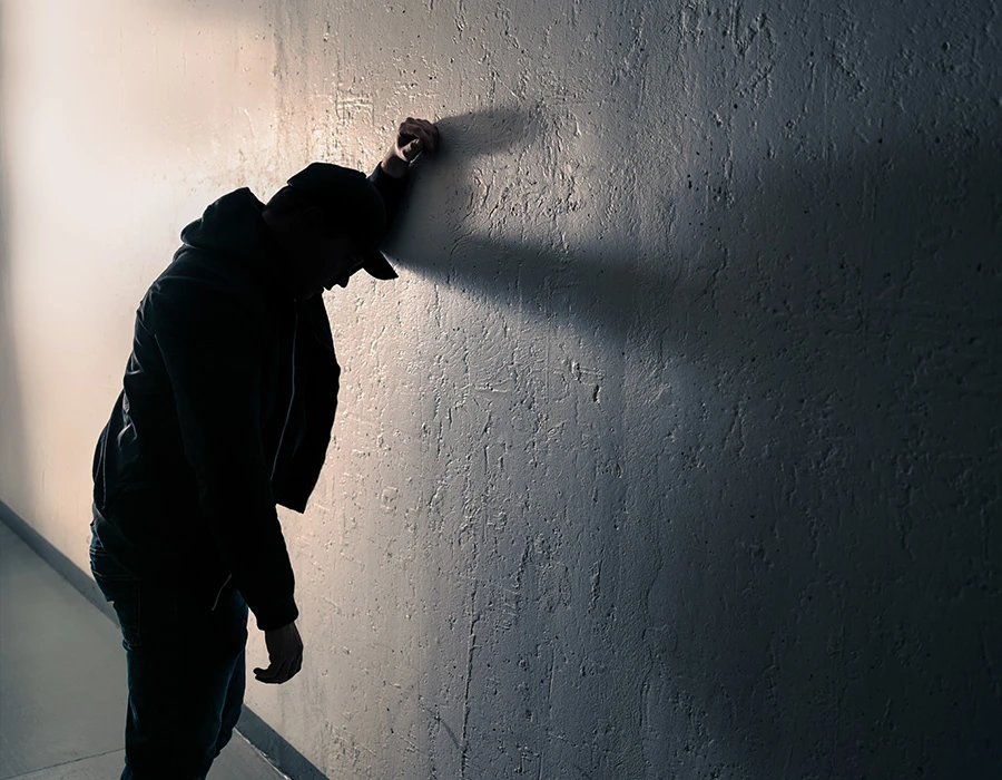 Persoon staat tegen muur en kijkt naar beneden als teken van twijfel over verslaving.