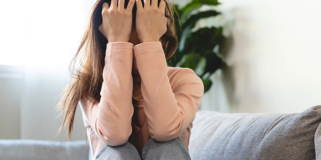 Vrouw zit op bank met handen in het haar, beeld van psychische stress en kwetsbaarheid.