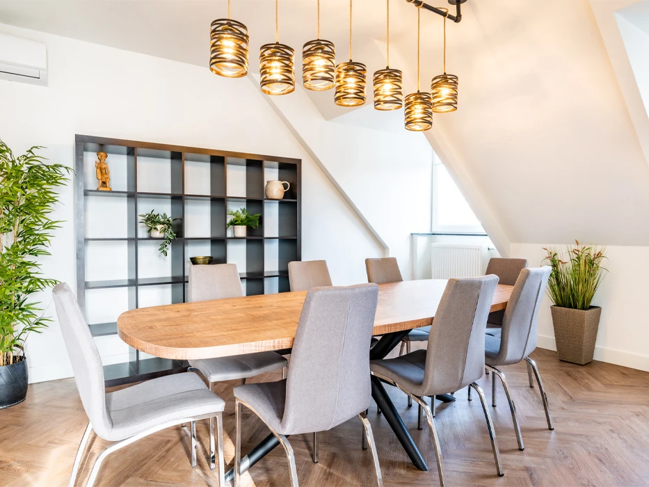 Vergaderruimte met ovalen tafel, 8 grijze stoelen en boekenkast tegen een witte muur op een visgraatvloer en planten verdeeld over de kamer.