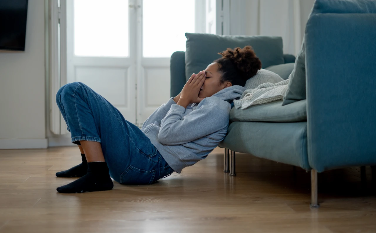 Vrouw zit op de grond met haar handen voor haar neus en mond en leunt met gesloten ogen tegen een bank doordat ze moet
afkicken van coke.