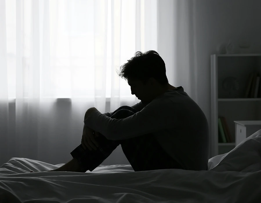 Silhouet van persoon op bed bij raam, sombere sfeer die depressie uitbeeldt.