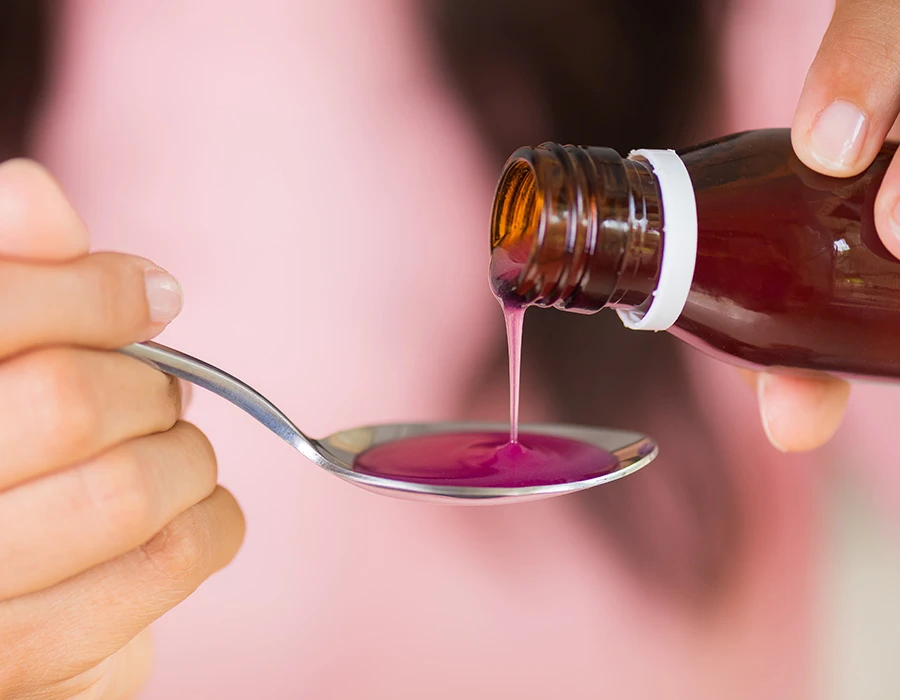 Roze-paarse siroop wordt uit een bruin flesje op een lepel geschonken, ter illustratie van lean.