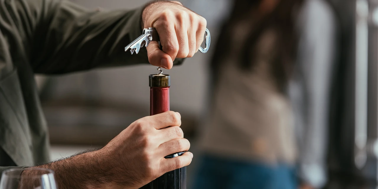 Man opent wijnfles met sleutel als voorbeeld van trucjes alcoholist.