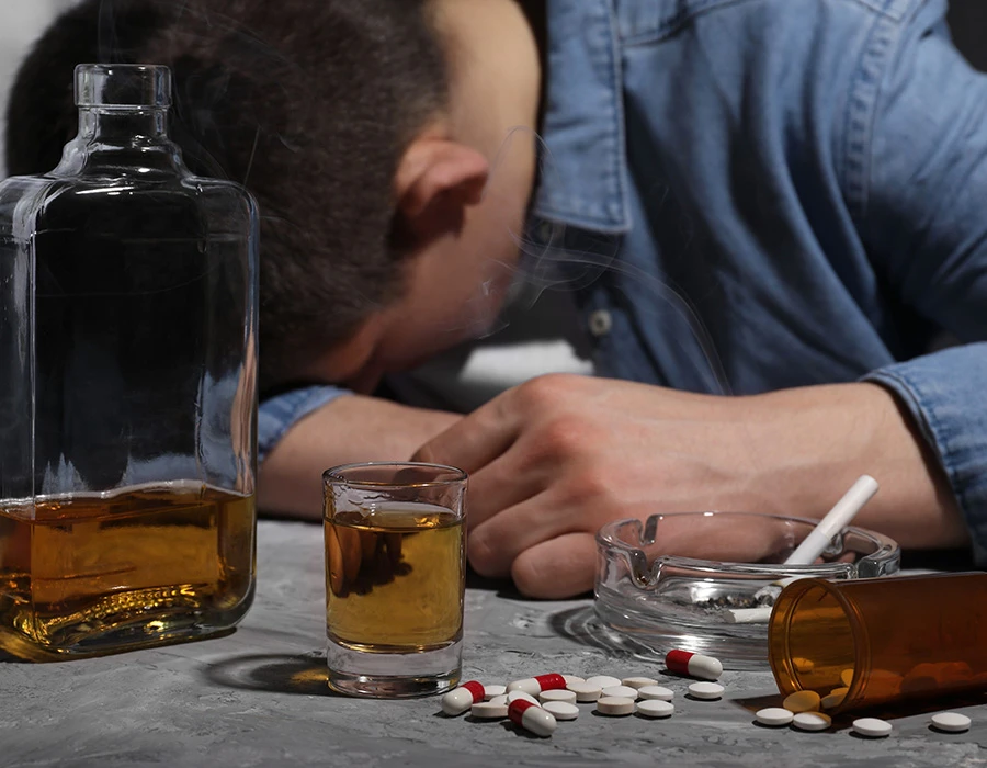Man ligt met hoofd op tafel is alcohol drugs zichtbaar met pillen en glas whisky.