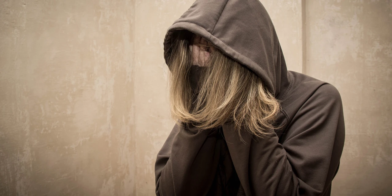 Persoon met capuchon zit ineengedoken en verbergt gezicht met handen.