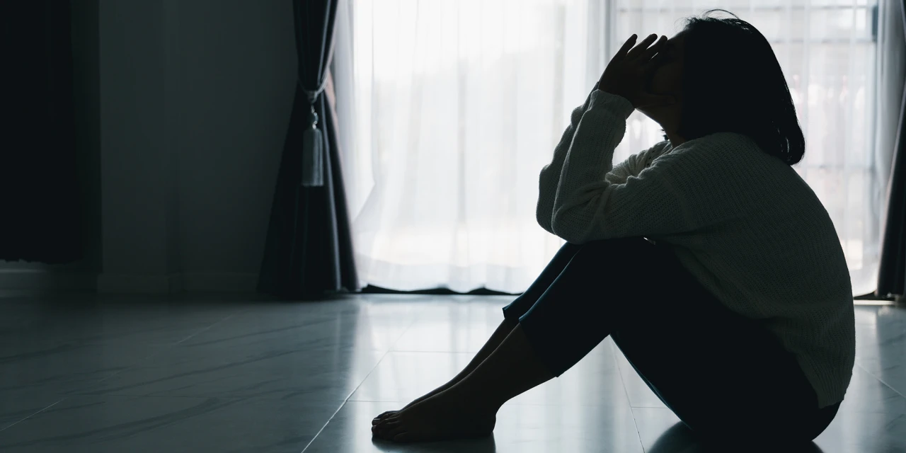 Persoon zit op de vloer bij een raam met hoofd in handen.