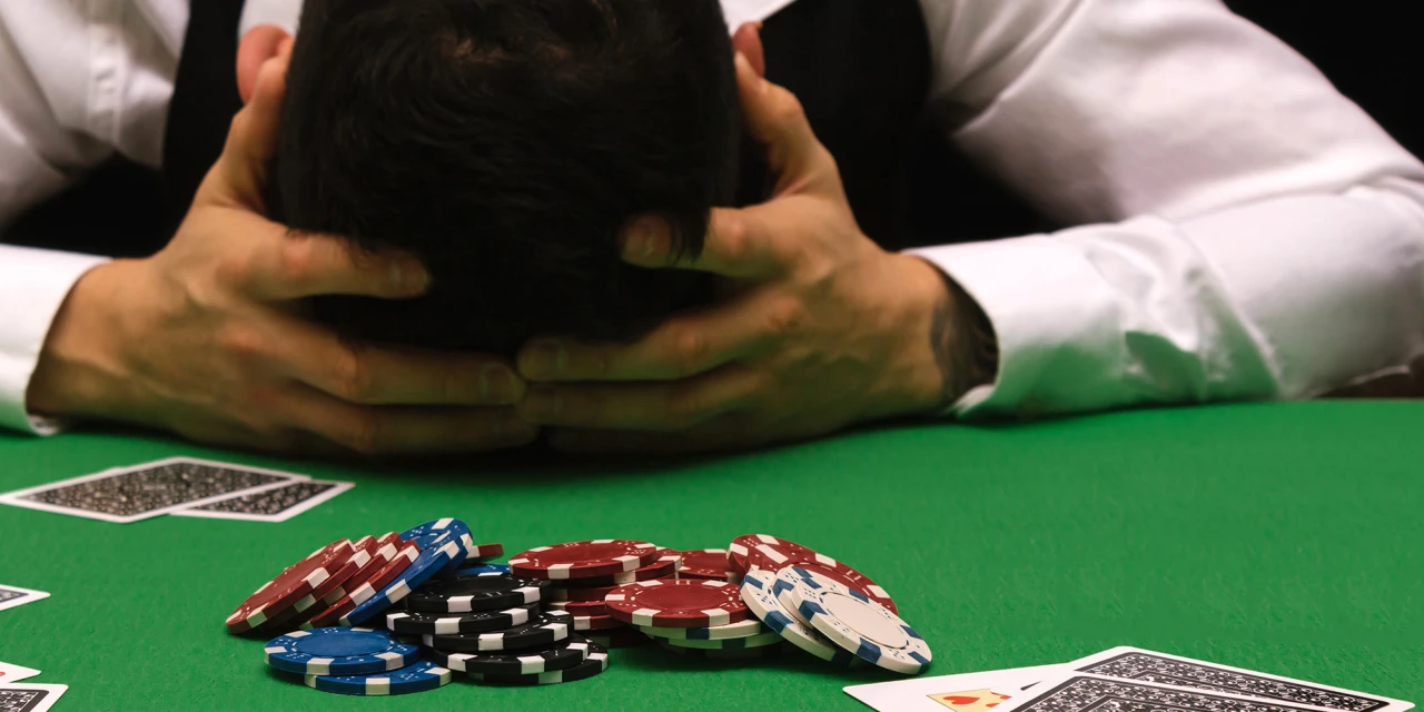 Man met hoofd in handen achter pokerfiches illustratie van wanhoop door gokverslaving.