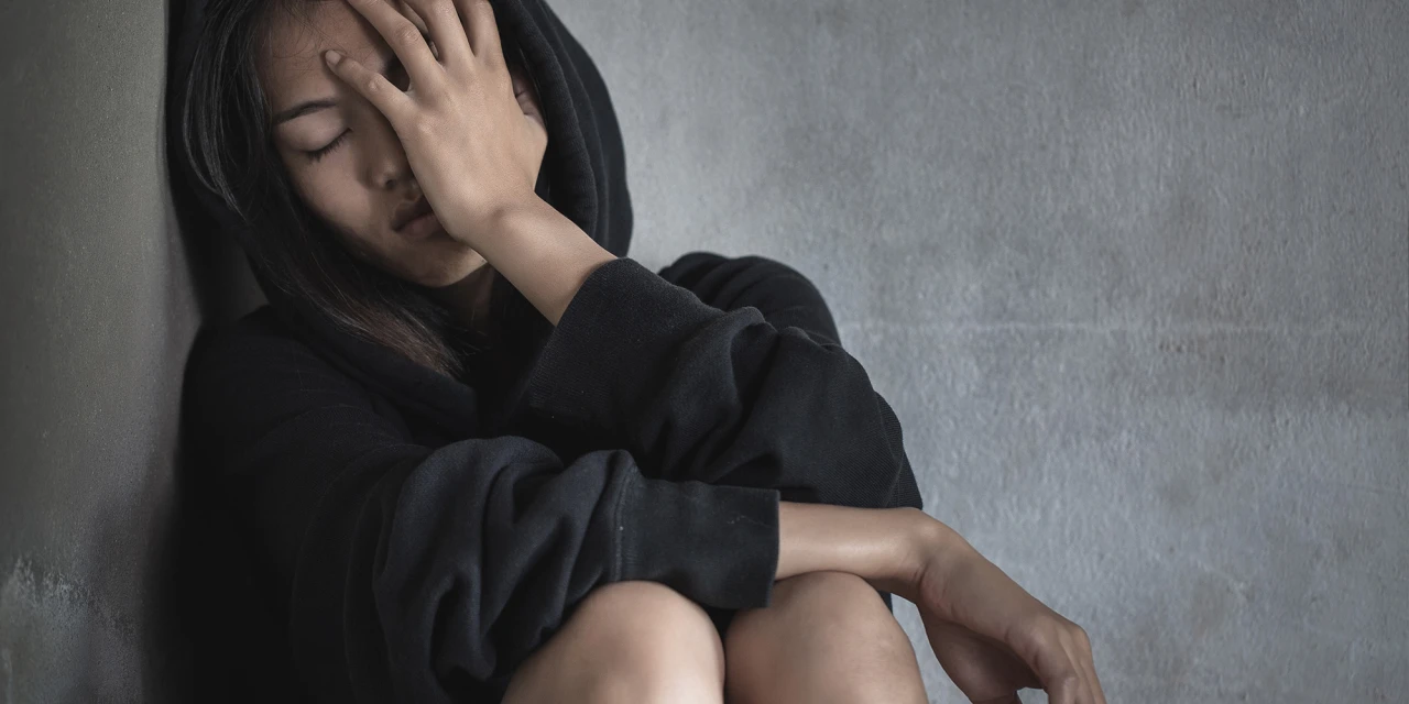 Vrouw zit tegen muur met hand op gezicht lijdend aan ontwenningsverschijnselen.