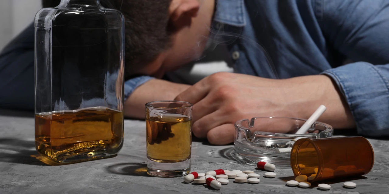 Een man ligt bewusteloos naast drank en pillen door overdosis.