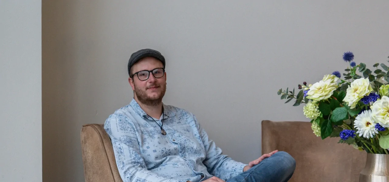 herstelverhaal-wesley Wesley, met pet, bril en baardje, vertelt zijn herstelverhaal terwijl hij in een bruine stoel zit.