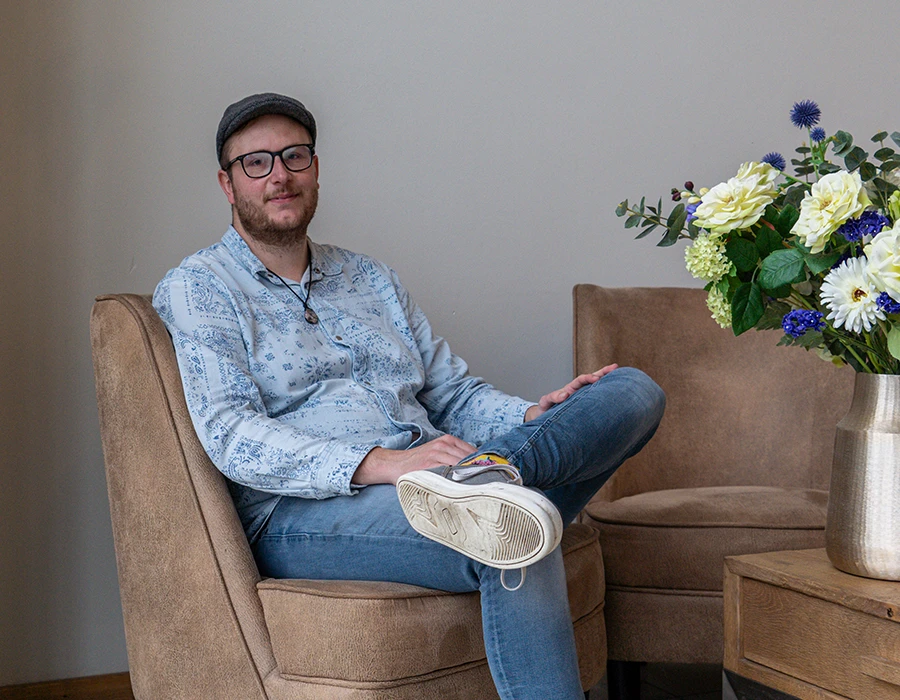 Wesley, met pet, bril en baardje, vertelt zijn herstelverhaal terwijl hij in een bruine stoel zit.