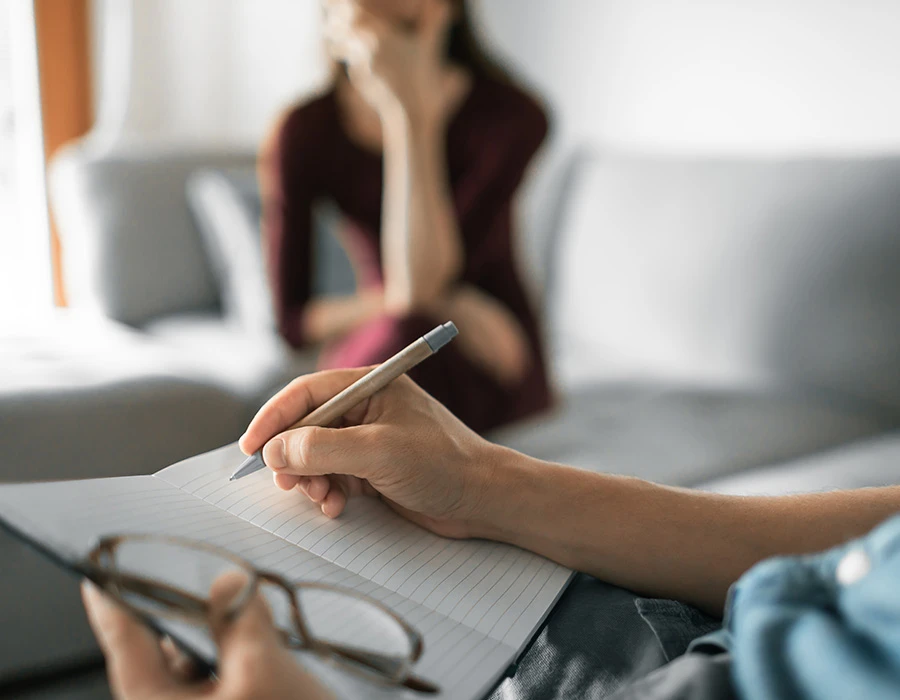 Psycholoog maakt aantekeningen tijdens gesprek met cliënt op de bank.