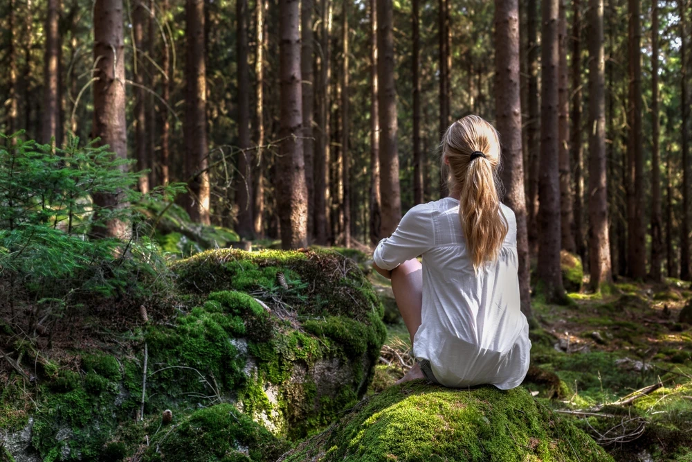 vrouw-in-bos Vrouw zit op een rotsblok in het bos te wachten.