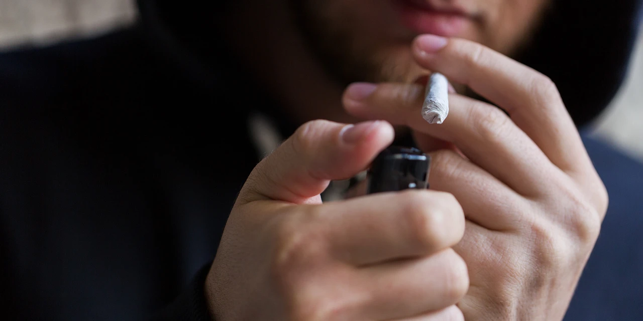 Behandeling cannabisverslaving persoon steekt joint aan met aansteker.