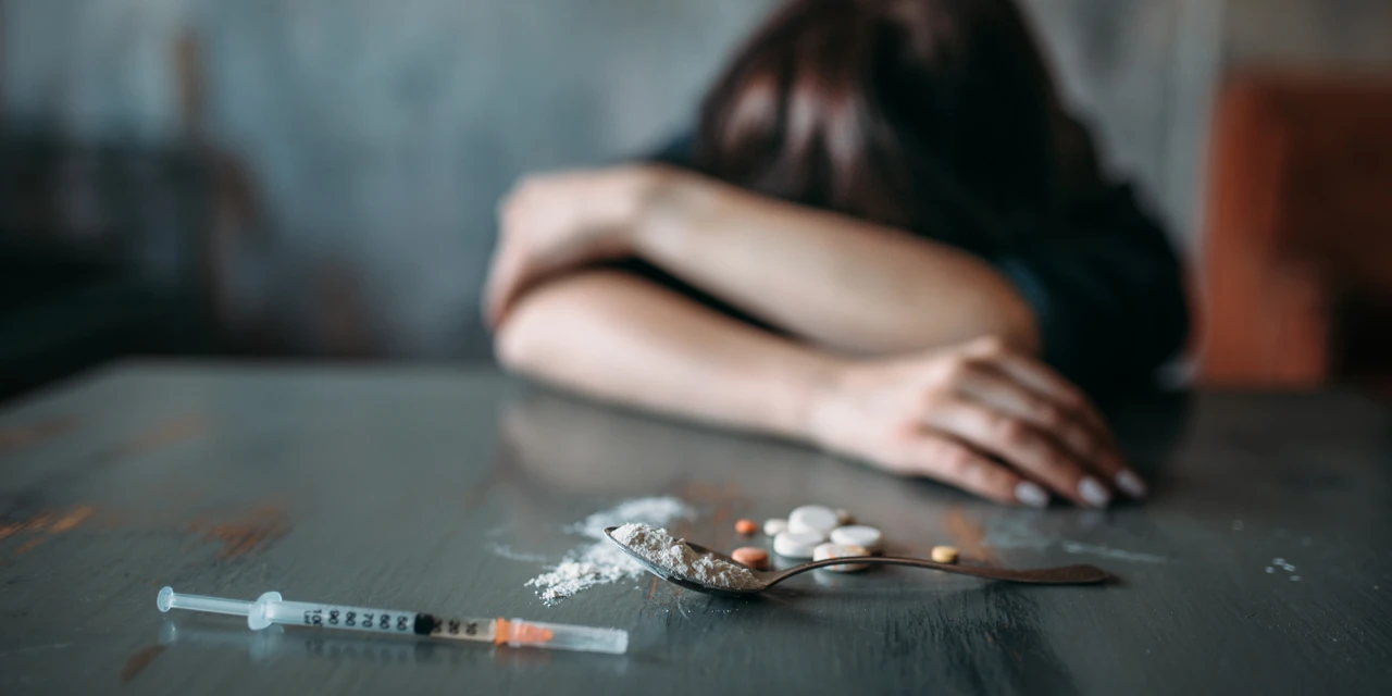 Persoon op tafel met spuit, poeder en pillen, gebruik van tranq drugs.