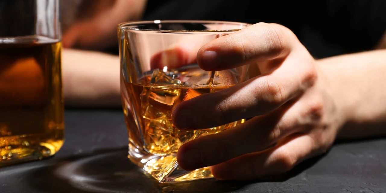 Hand houdt glas alcohol vast met ijsblokjes, symbool voor drinken.