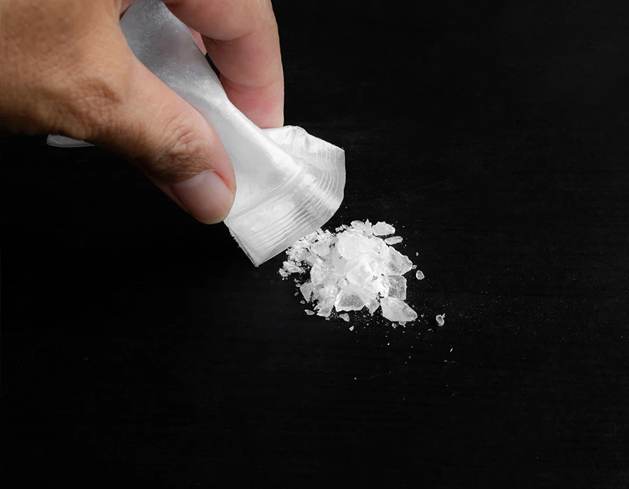 Witte amfetaminekristallen worden uit zakje op tafel gestrooid.
