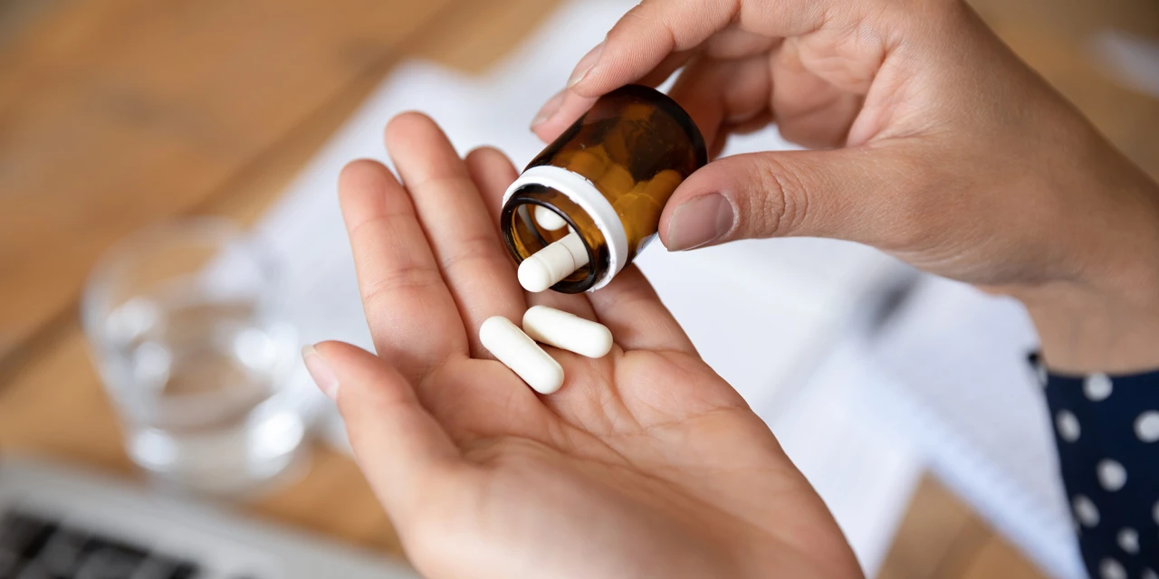 Tabletten uit medicijnflesje in hand, beeld van gebruik van pijnstillers.