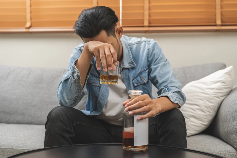 Man zit somber op bank met glas drank, symbool voor alcoholgebruik en alcoholmisbruik.