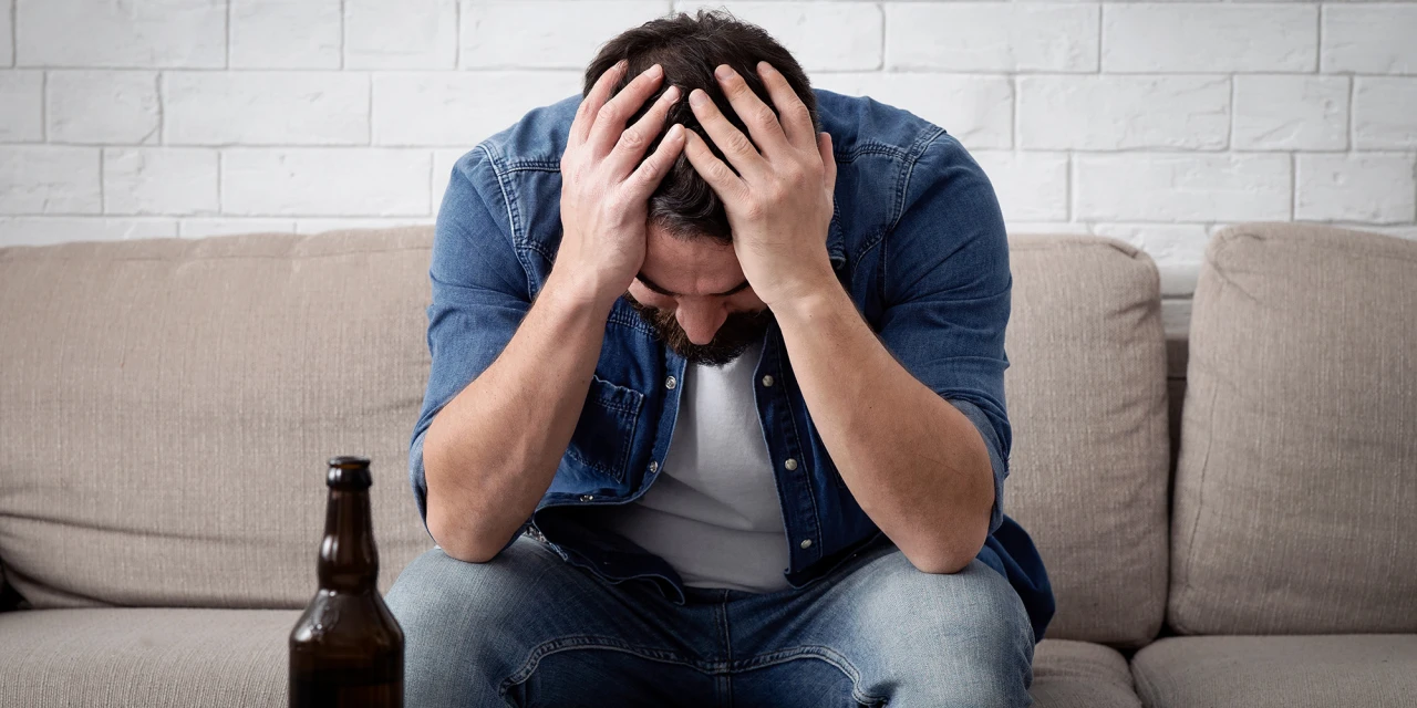 Man zit op de bank met bierfles en denkt aan stoppen met alcohol.