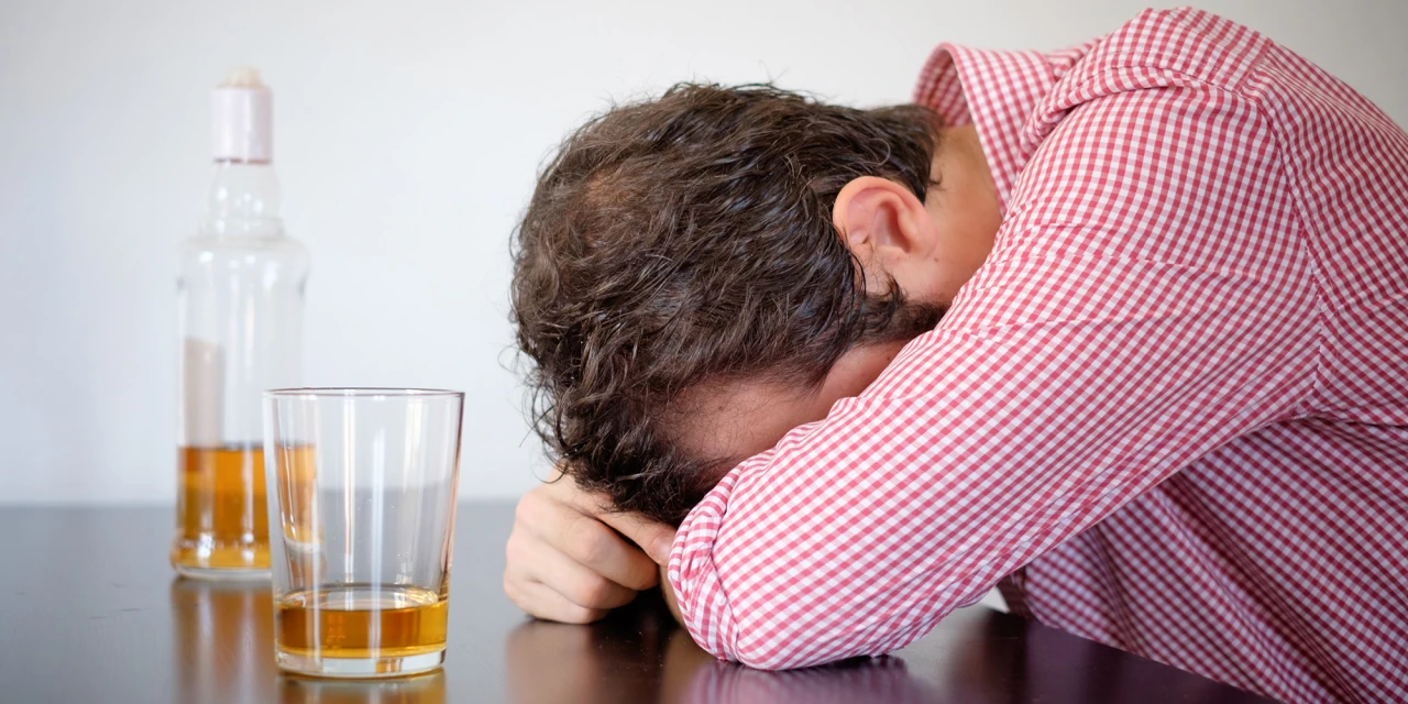 Man met hoofd op tafel naast glas drank, symbool voor cold turkey stoppen met alcohol.