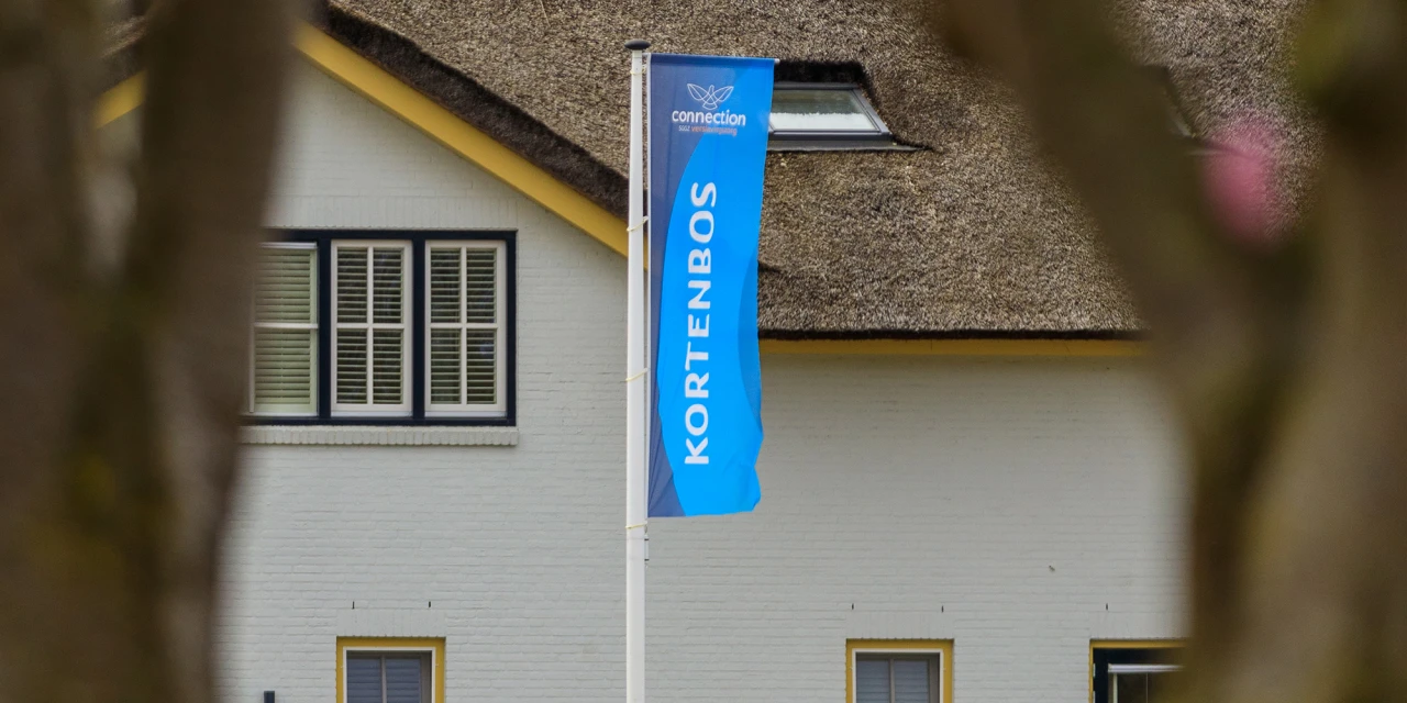 Blauwe vlag bij afkickkliniek Meerlo voor gebouw met rieten dak.