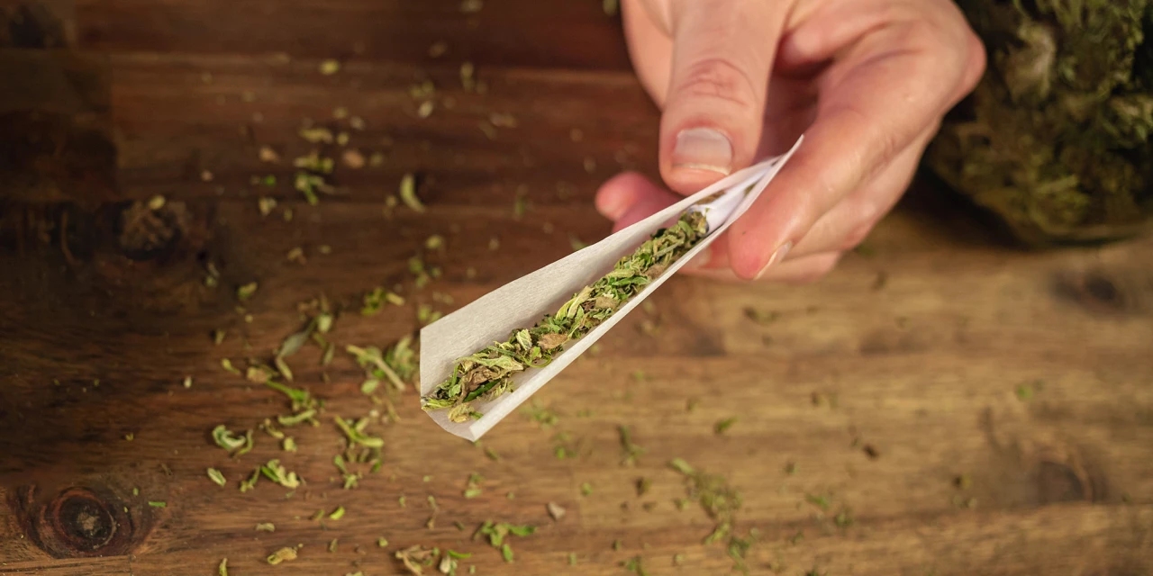 Een hand rolt een joint met cannabis en laat stap voor stap zien wat is cannabis.