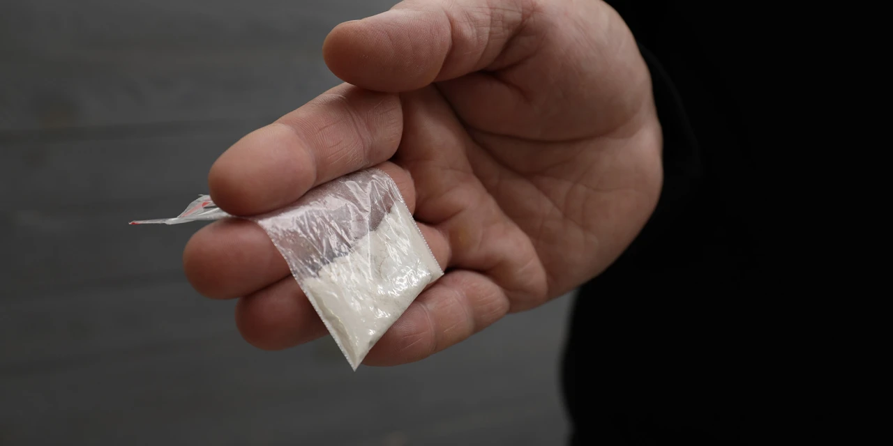 Hand houdt zakje met wit poeder vast. Wat is coke?