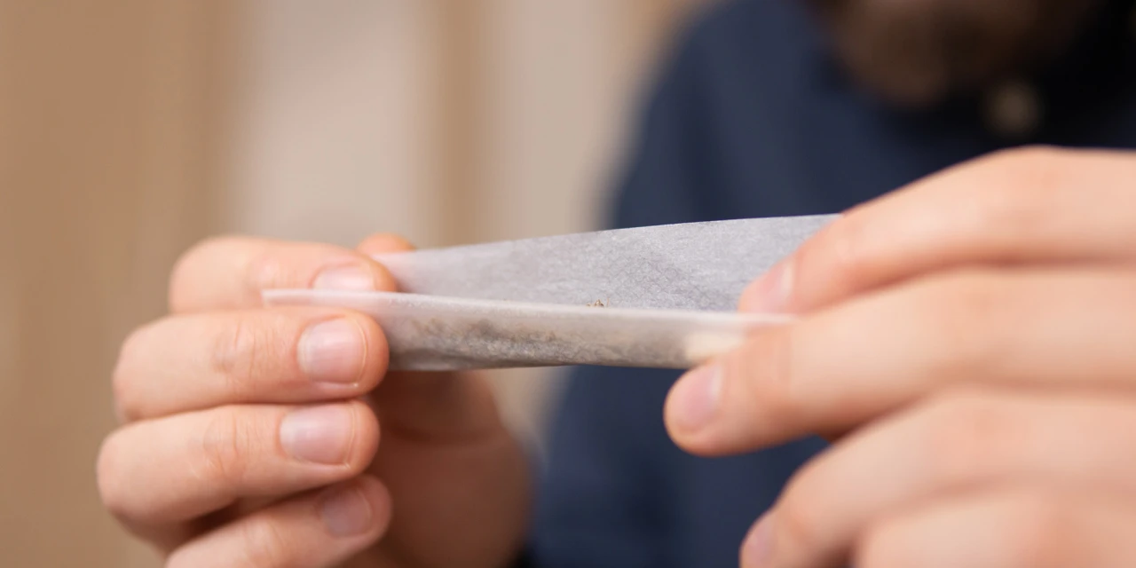 Handen rollen een joint van papier met softdrugs cannabis erin.
