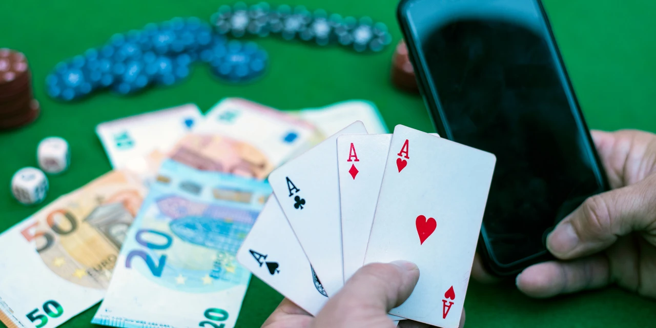 Hand houdt vier azen en smartphone geld op tafel. Illustratie van gokverslaving.