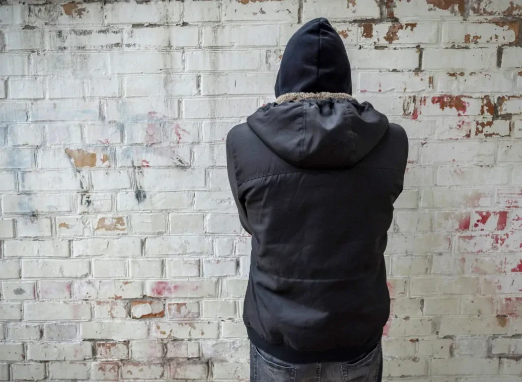 depressieve-man-kijkt-naar-muur Depressieve man met donkere capuchon op kijkt naar muur en staat met de rug naar de kijker.