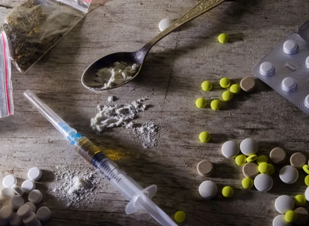 soorten-harddrugs-en-softdrugs Allerlei harddrugs en softdrugs, zoals pillen, injectienaalden en zakjes wiet, liggen op tafel.