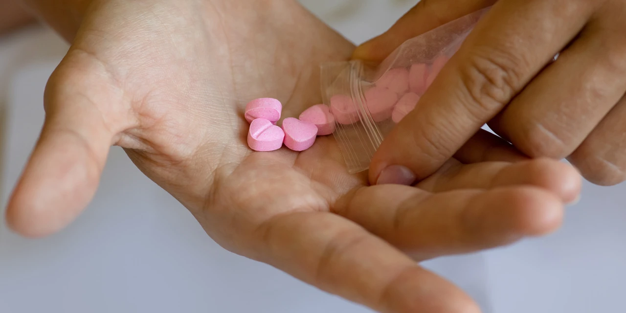 Wat is MDMA? Roze hartvormige pillen uit een zakje in een hand.