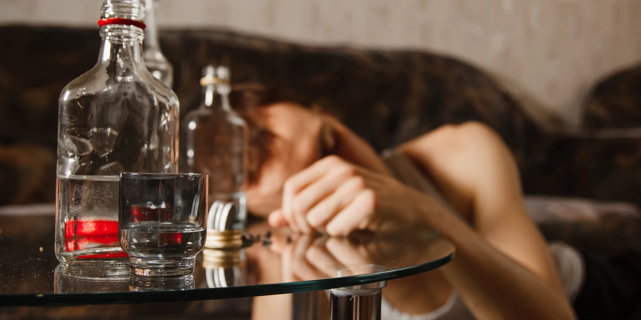 Persoon ligt op bank met hand op tafel lijdend aan ontwenningsverschijnselen van alcohol.