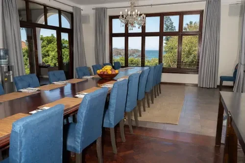 zuid-afrika-vergaderruimte Ruimte van afkickkliniek Zuid-Afrika, met lange houten tafel, blauwe stoelen en uitzicht op de zee.