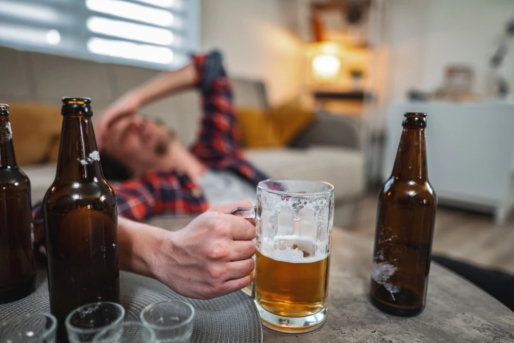 Man ligt dronken op bank met bierflessen en glas tijdens comazuipen.